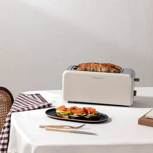Toaster on a table with bread and a plate of food, against a white wall.
