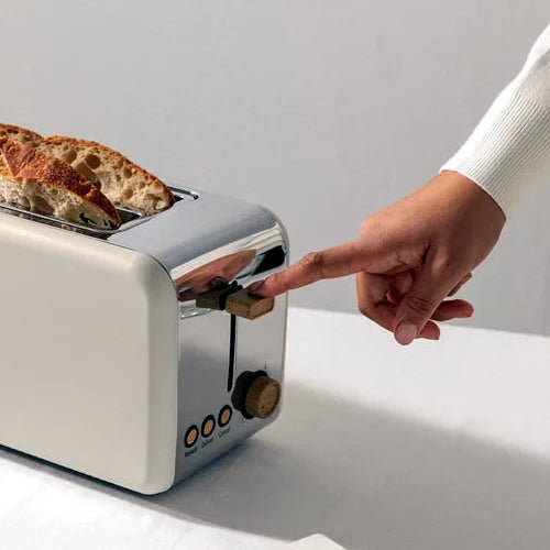 Person adjusting a toaster with bread inside on a light surface.
